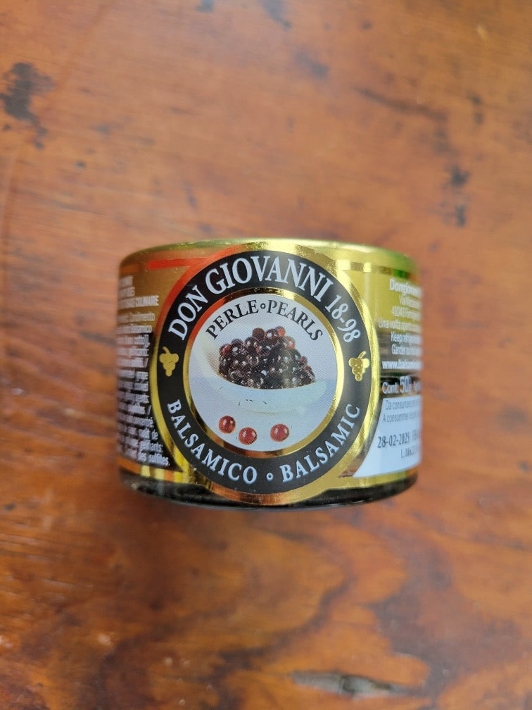 Balsamic pearls arranged on a plate with a spoon beside them. The pearls are small, round, and uniform, with a dark red hue, resembling caviar. The plate is white with a blurred background, showcasing the elegant and delicate appearance of the Balsamic Pearls by Don Giovanni Ponte Vecchio.